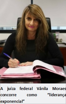 foto vertical mulher branca sentada em uma cadeira com uma mesa na sua frente ela olha para câmera enquanto segura uma caneta para assinar um documento. juiza federal Vânila Moraes concorre como liderança exponencial.