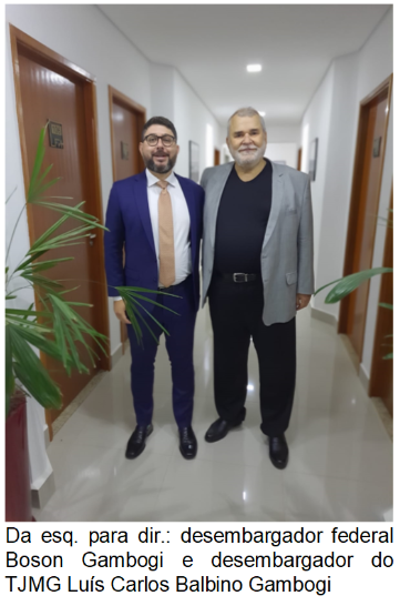 Fotografia vertical colorida dois homens em pé em um corredor. Legenda: desembargador federal Boson Gambogi e desembargador do TJMG Luís Carlos Balbino Gambogi.