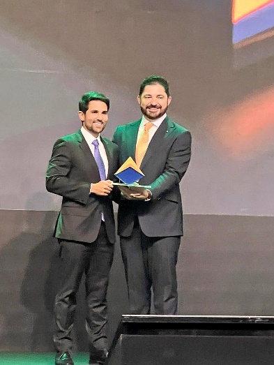 Fotografia vertical colorida homem entregando troféu a outro homem.