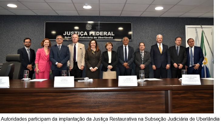 Fotografia horizontal colorida pessoas em pé, lado a lado, atrás da mesa em um auditório. Legenda: autoridades participam da implantação da Justiça Restaurativa na Subseção Judiciária de Uberlândia.