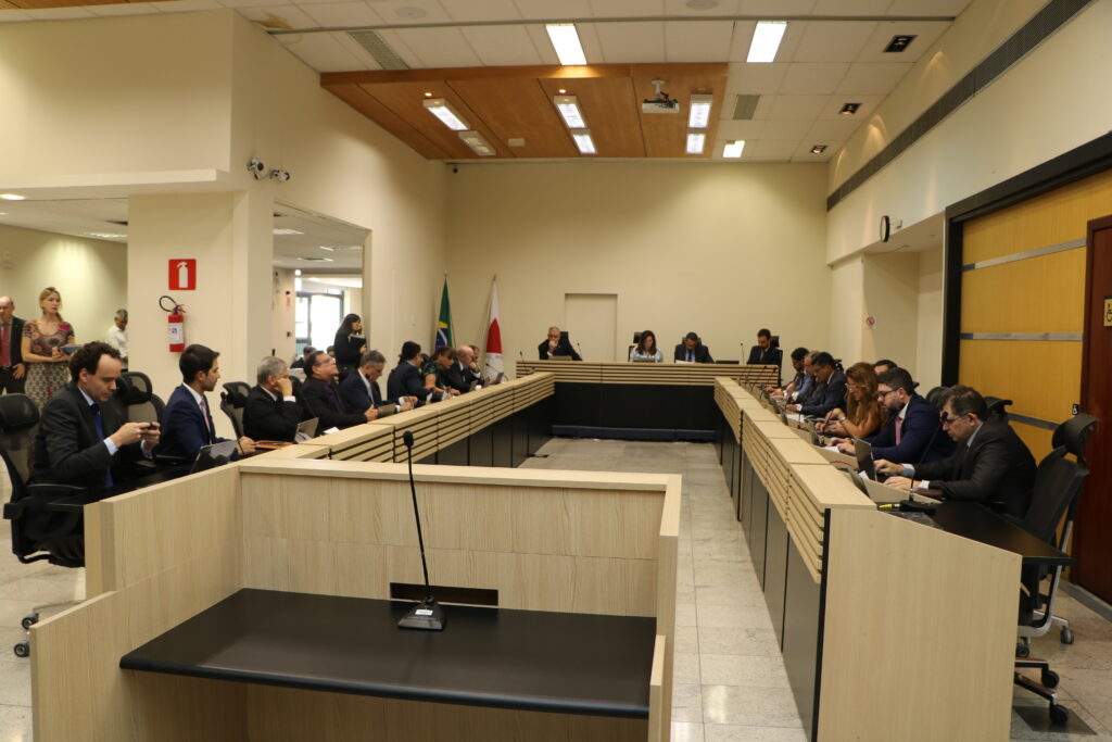 Fotografia arredondada colorida pessoas sentadas em uma sessão plenária no TRF6.