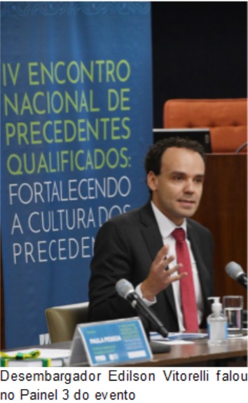 Fotografia retangular e colorida de um homem de terno gesticulando numa mesa com microfone. Ao fundo, lê-se "IV Encontro Nacional de Precedentes Qualificados: Fortalecendo a Cultura dos Precedentes".