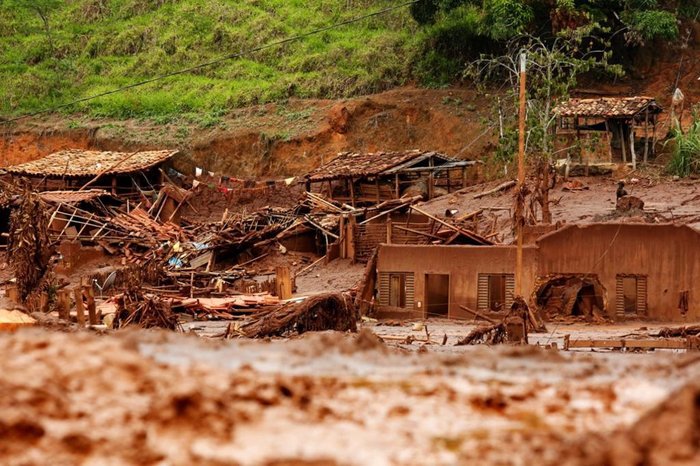 Fotografia retangular e colorida em que destroços de casas se encontram soterrados por lama.