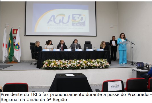 Foto colorida horizontal mostra a Presidente do TRF6 em pé fazendo um pronunciamento diante de uma tribuna. Ao lado, as demais autoridades aparecem sentadas na mesa de honra olhando em direção à desembargadora. 