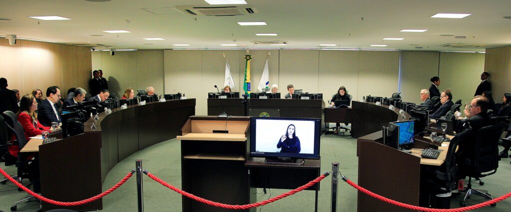 Fotografia retangular e colorida em que   magistrados se encontram reunidos ao redor de uma mesa semicircular.