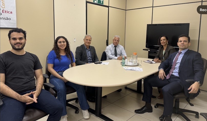 Quatro homens e duas mulheres sentados em torno da mesa de trabalho.